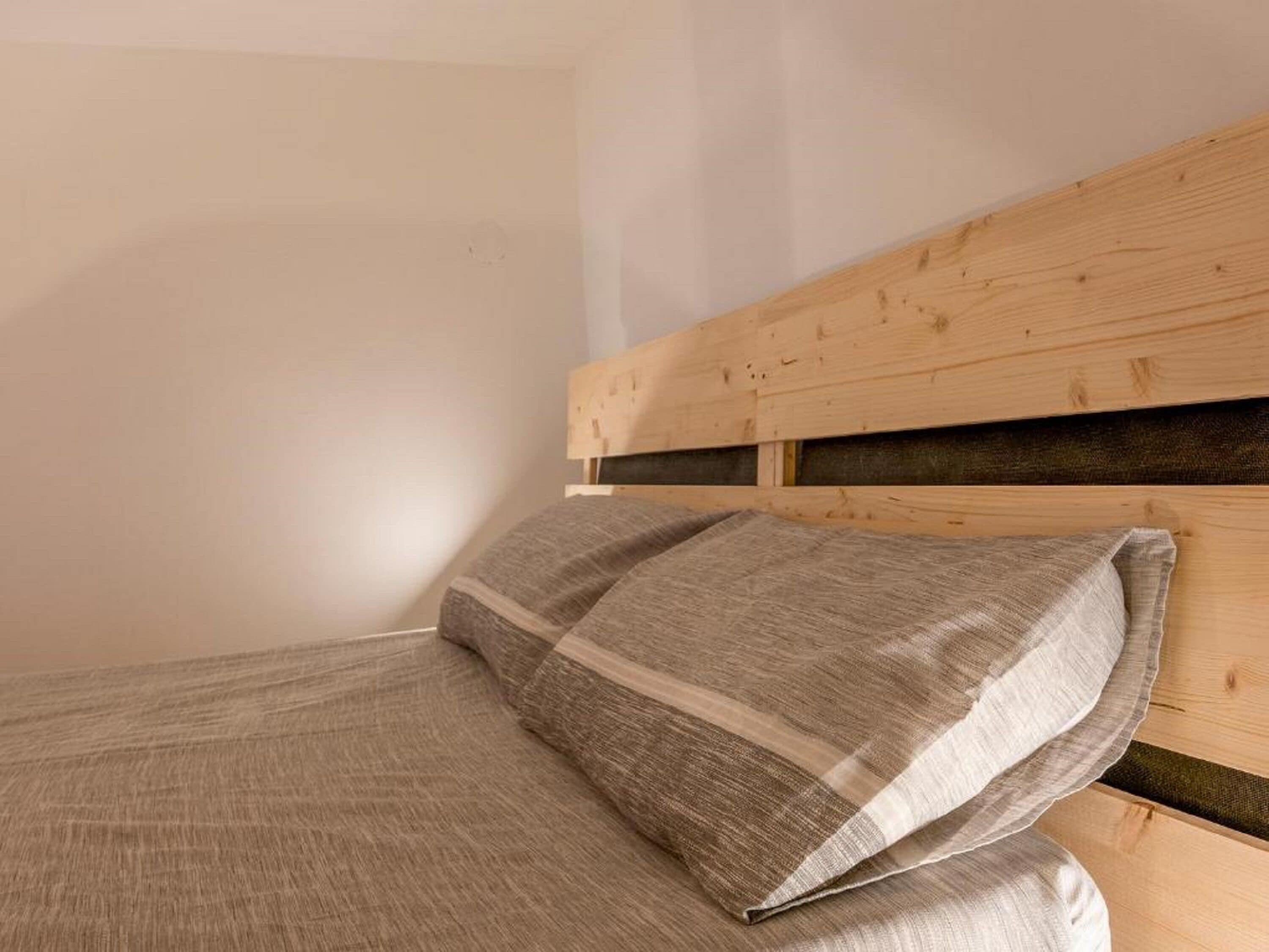 Ein Bett mit einem Holz-Kopfstück und einem grau gestreiften Kopfkissen.