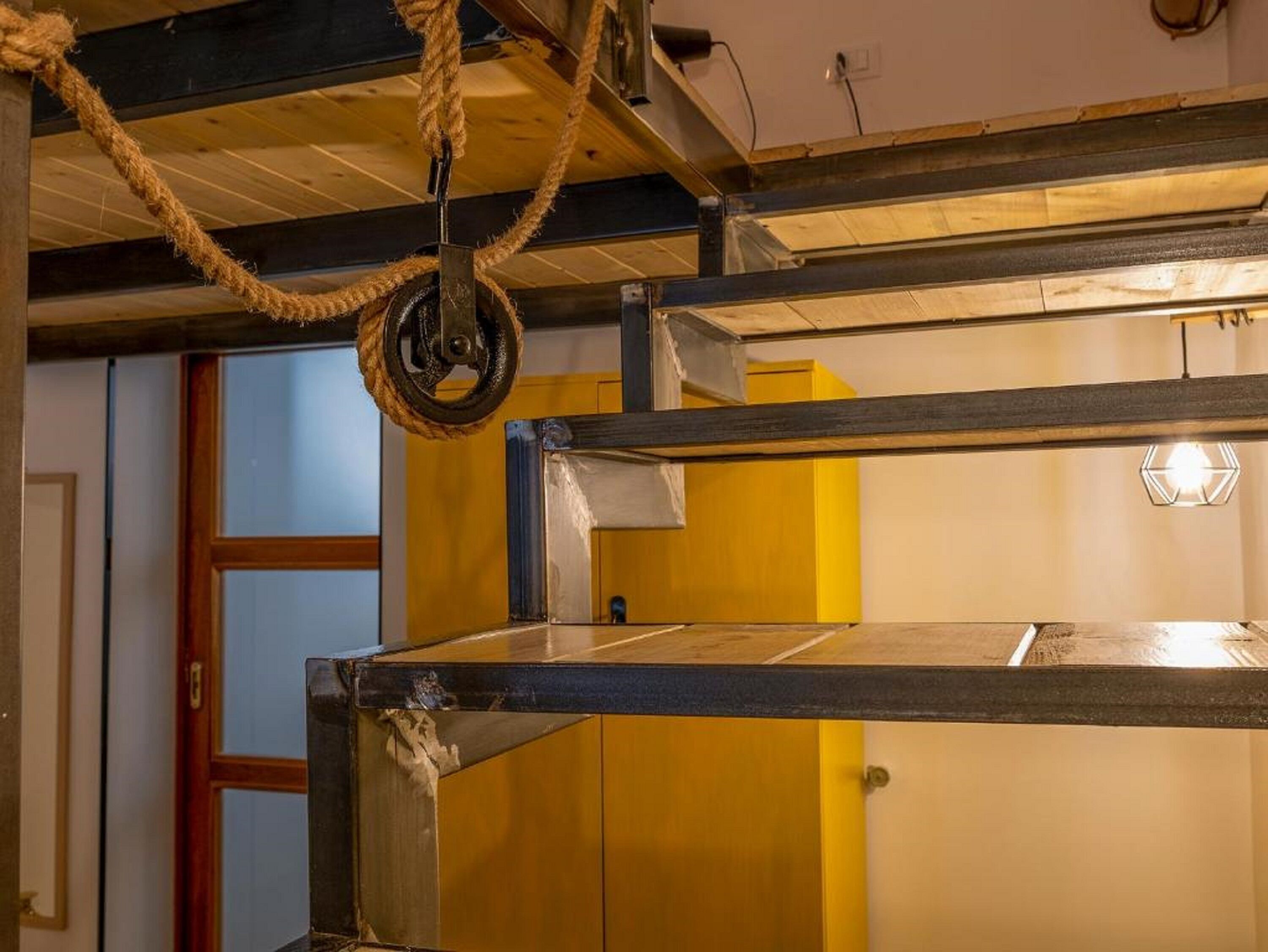 Una litera con una cuerda atada al techo, una puerta de madera y una pared amarilla.