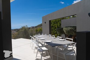 An outdoor dining area with a table set for six, surrounded by white chairs, against a modern building with a view of the countryside. - CostaBlancaDreams - Perla in Calpe (Calpe)