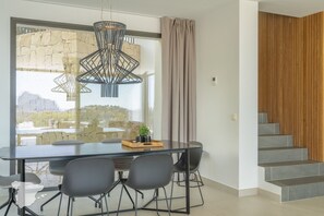 A modern dining area with a stone wall, a hanging light fixture, and a staircase with wooden paneling. - CostaBlancaDreams - Perla in Calpe (Calpe)