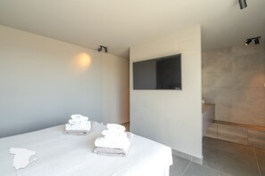 A hotel room with a bed, a flat-screen TV mounted on the wall, and a bathroom with a shower.