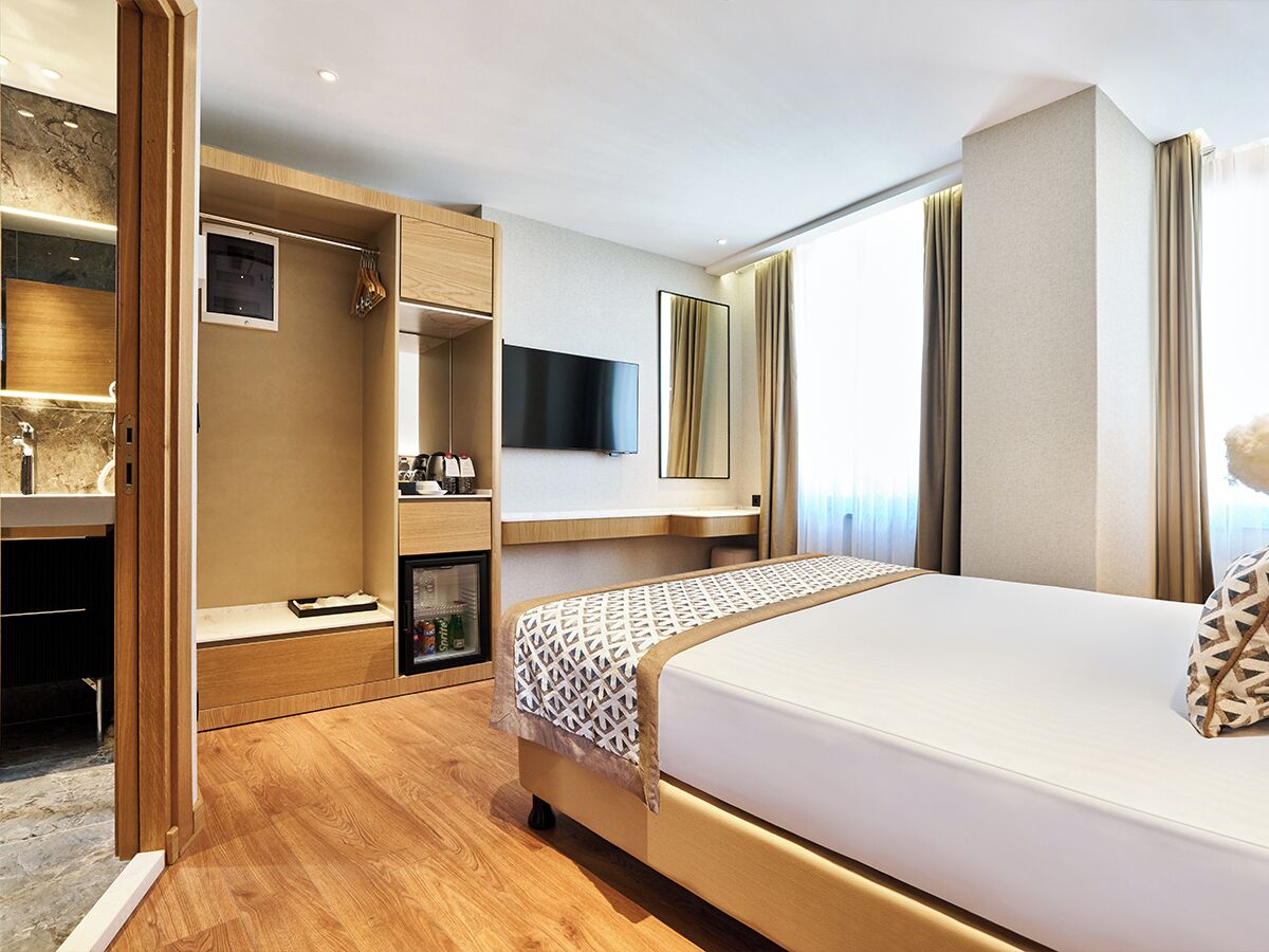 A modern hotel room with a large bed, a built-in wardrobe, a flat-screen TV, and a minibar.