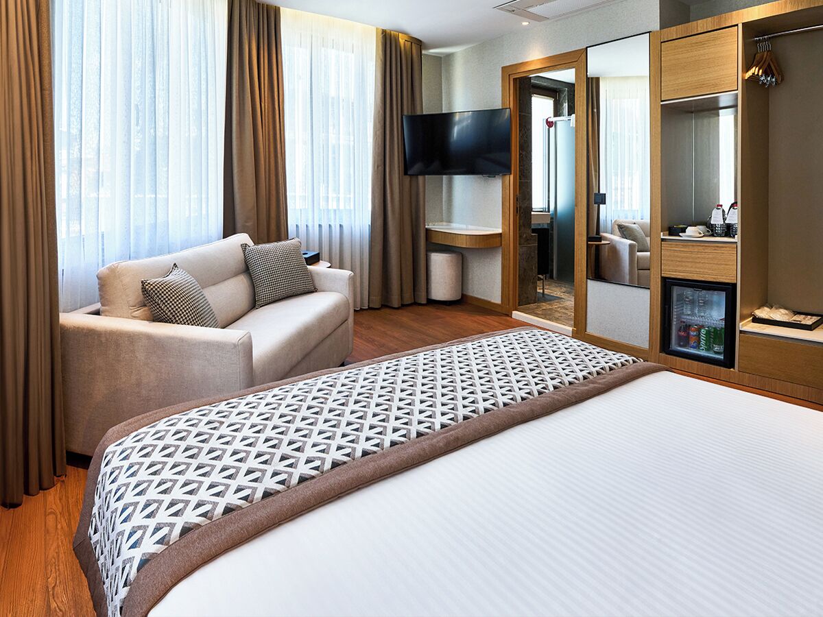 Hotellihuone, jossa on suuri sänky, sohva, televisio, peili ja minibaari.