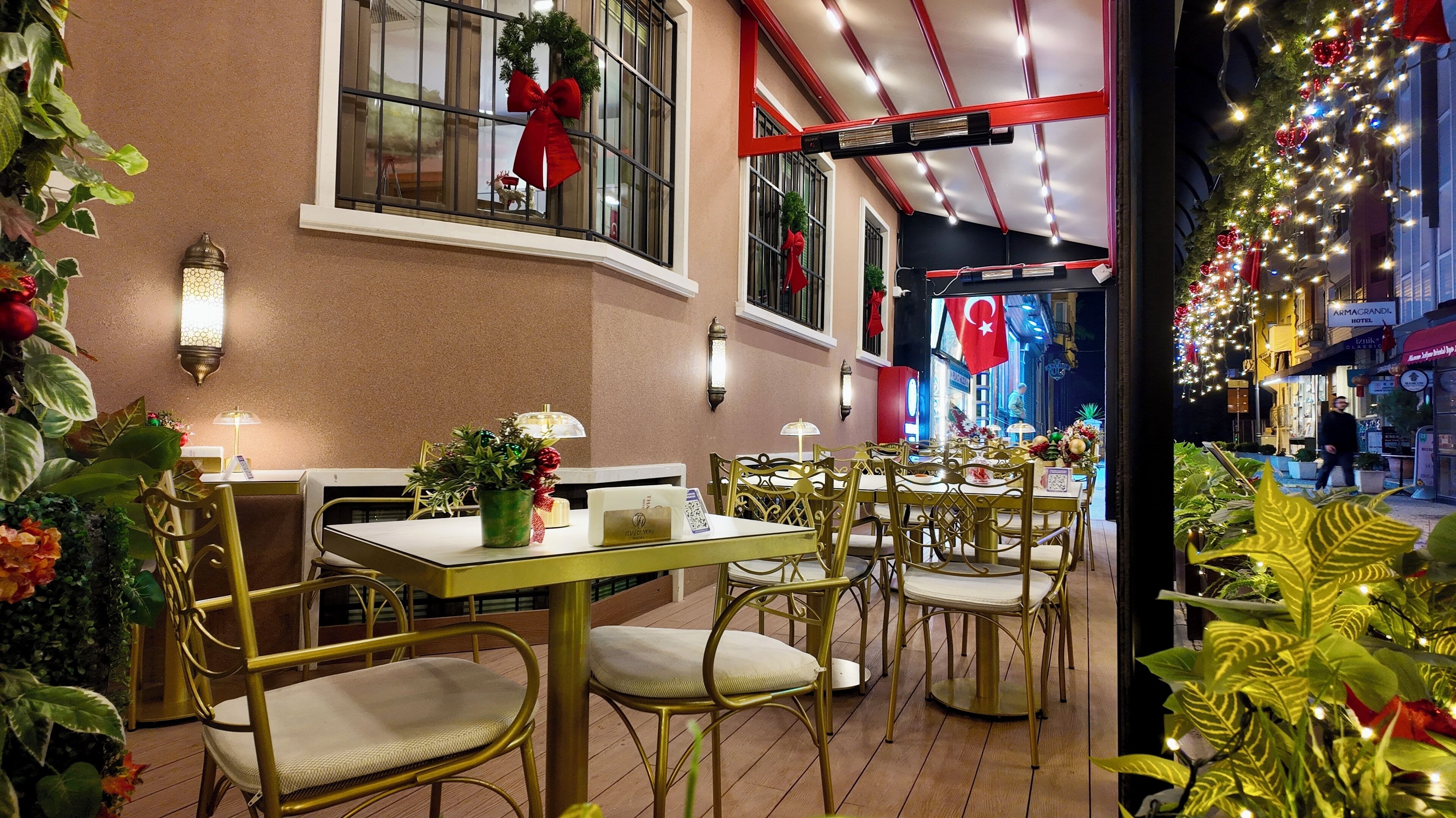 An outdoor dining area with tables and chairs, decorated with plants and holiday ornaments.