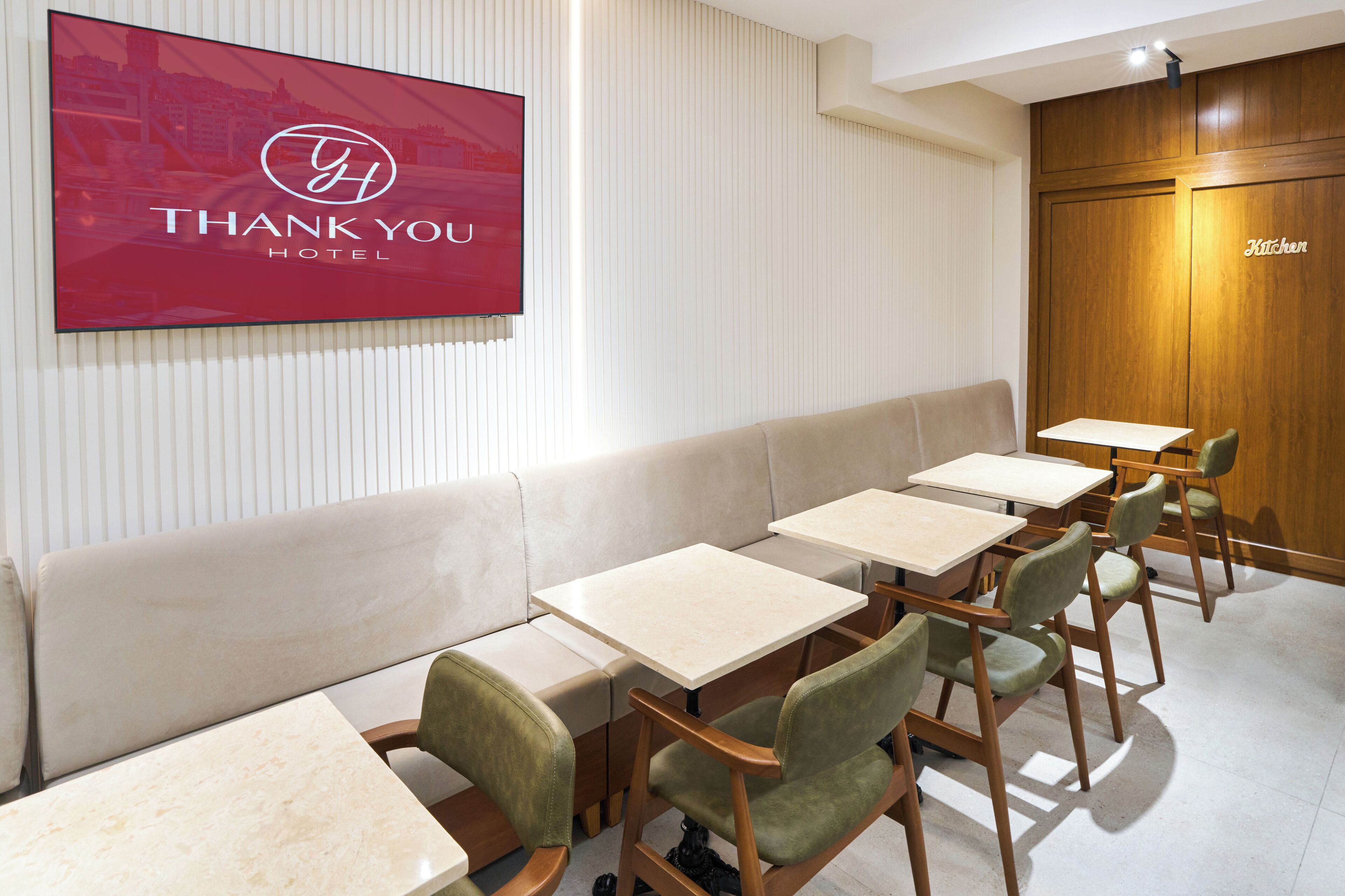 A hotel lobby with a reception desk, a seating area with tables and chairs, and a wall-mounted TV displaying the hotel's logo.