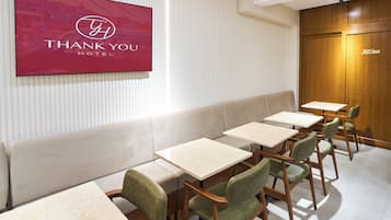 A hotel lobby with a reception desk, a seating area with tables and chairs, and a wall-mounted TV displaying the hotel's logo.