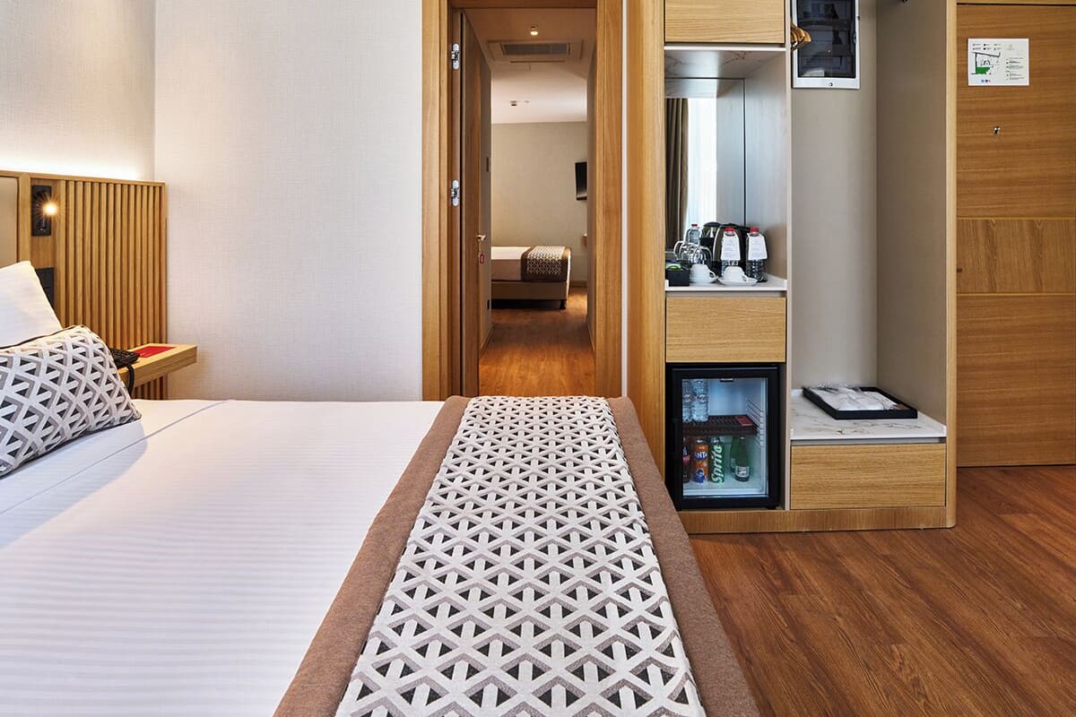 A hotel room with a bed, a small kitchenette, a wardrobe, and a door leading to a hallway.