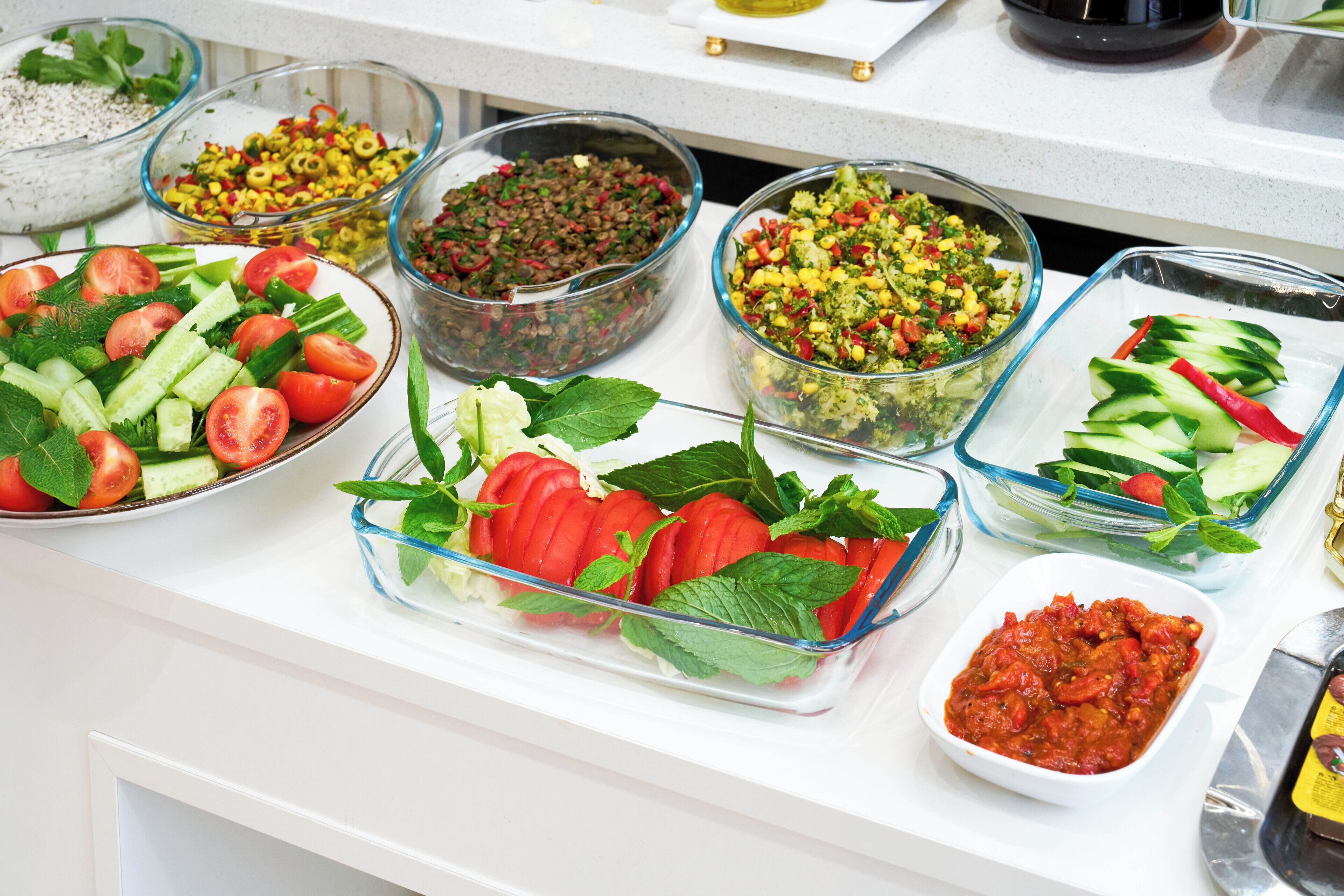 A buffet table with various dishes including salads, vegetables, and a bowl of tomato sauce.