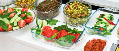 A buffet table with various dishes including salads, vegetables, and a bowl of tomato sauce.