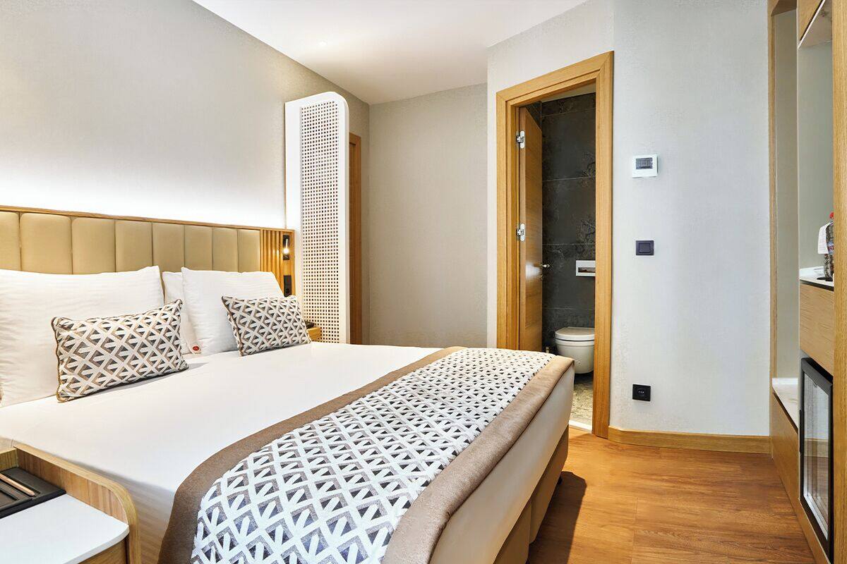A hotel room with a large bed, wooden headboard, and a bedside table.