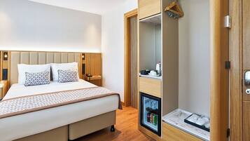 A modern hotel room with a bed, a wardrobe with a built-in mini-fridge, and a small bedside table.