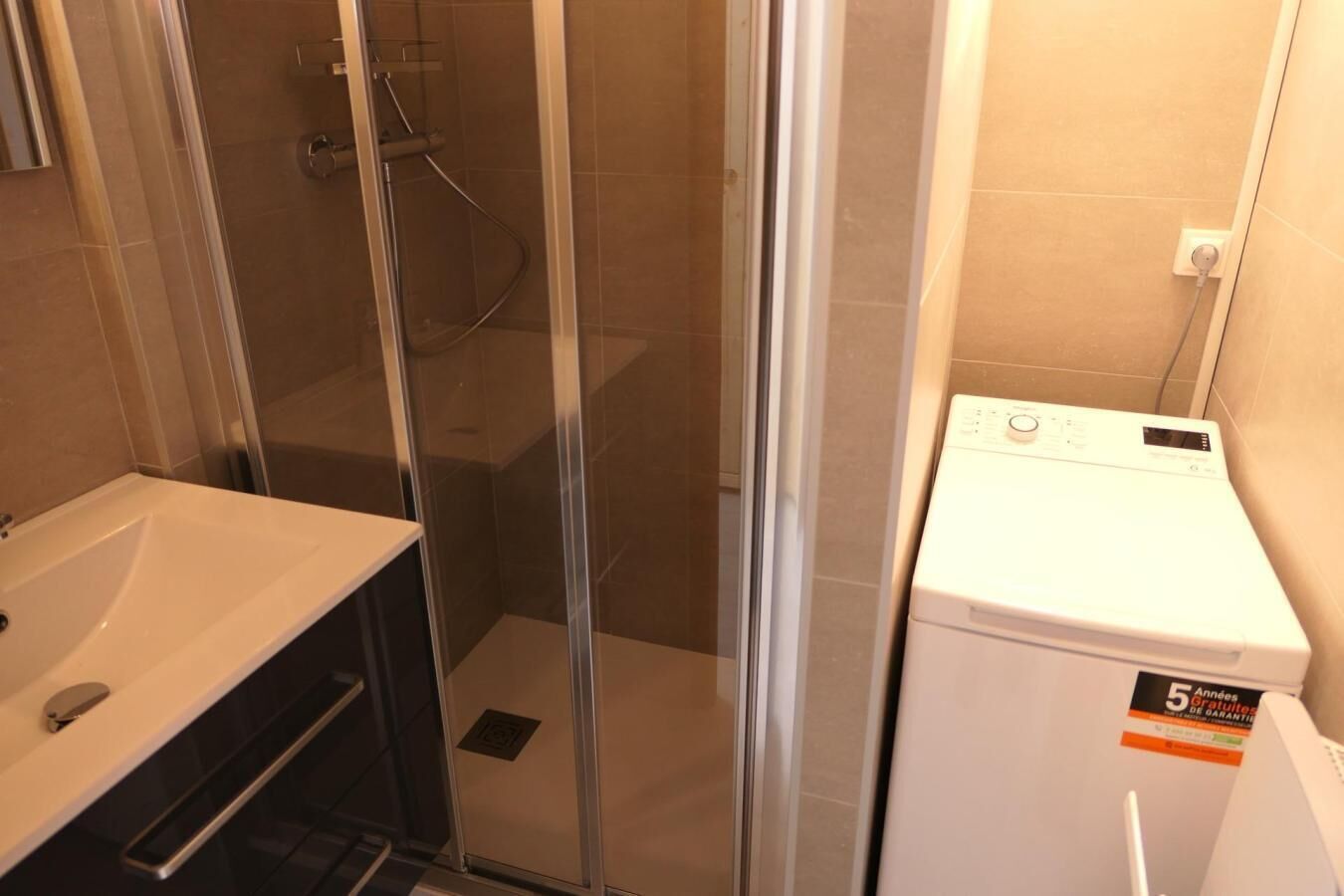 Un baño con ducha de vidrio, lavamanos y lavadora blanca.