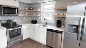 A modern kitchen with white cabinets, stainless steel appliances, a microwave, toaster, coffee maker, and a refrigerator. - Beechwood by the Bay Dog Friendly (Lower Township)
