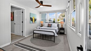 A bedroom with a bed, a ceiling fan, a window with a view, and a door leading to another room. - Lux Seaside Retreat Steps to Beach (Lower Township)
