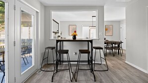 A modern kitchen with a central island, bar stools, and a dining area with a table and chairs. - Lux Seaside Retreat Steps to Beach (Lower Township)
