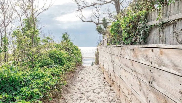 A sandy path leading to a beach, flanked by greenery and a wooden fence. - Lux Seaside Retreat Steps to Beach (Lower Township)