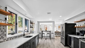 A modern kitchen with a large island, black appliances, and a view of the outdoors. - Lux Seaside Retreat Steps to Beach (Lower Township)