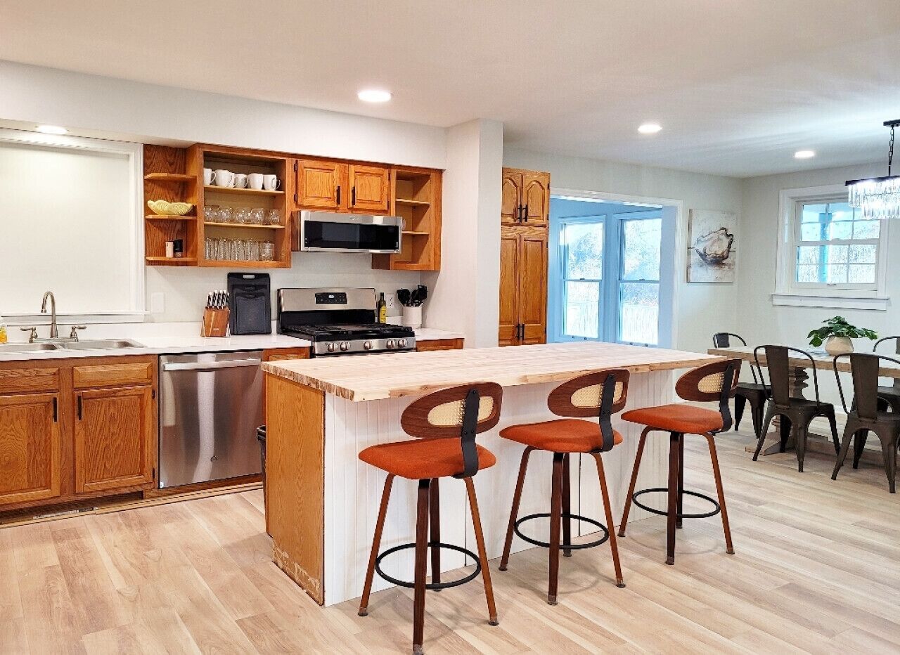 A modern kitchen with wooden cabinets, a stainless steel dishwasher, and a central island with bar stools.