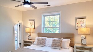 Ein Schlafzimmer mit einem Bett, zwei Nachttischen, einem Deckenventilator, einem Fenster und Wandbildern.