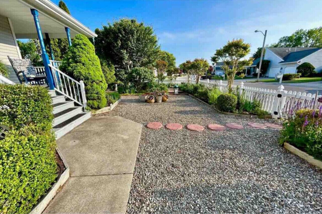 A residential driveway with a gravel path, a concrete walkway, and a white picket fence.