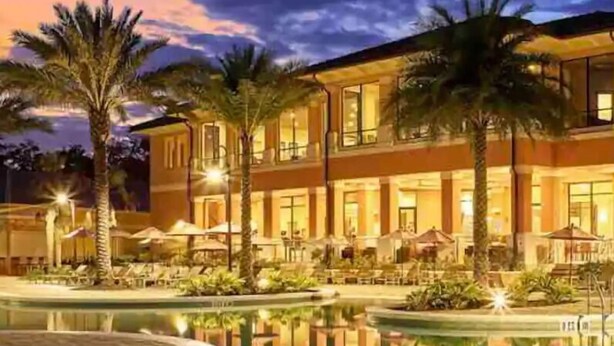 Um hotel com uma piscina grande, palmeiras e área externa bem iluminada.