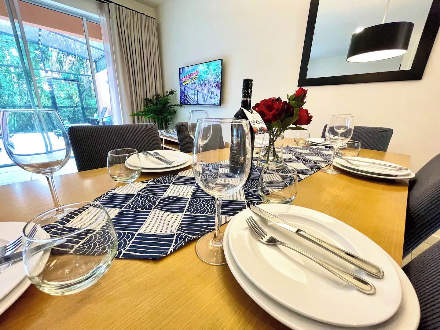 A dining table set with plates, glasses, and cutlery, a vase with red flowers, and a bottle of wine.