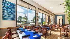 Uma sala de jantar ampla com grandes janelas, mesas e cadeiras de madeira.
