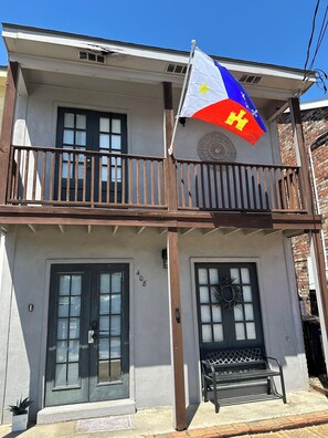 Un edificio de dos plantas con un balcón, una bandera y el número '408' en la pared.