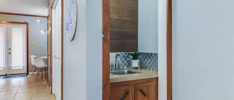 A hallway with a wooden door leading to a kitchen area with a sink and countertop.