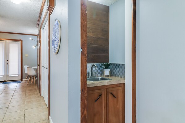A hallway with a wooden door leading to a kitchen area with a sink and countertop.