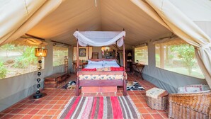 Ein Zeltraum mit Himmelbett, Teppich, Korbmöbeln und einer Lampe.