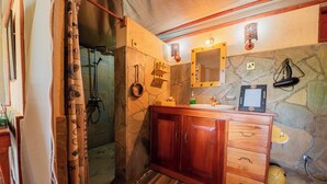 A bathroom with a shower, a wooden vanity, a mirror, and a stone wall.