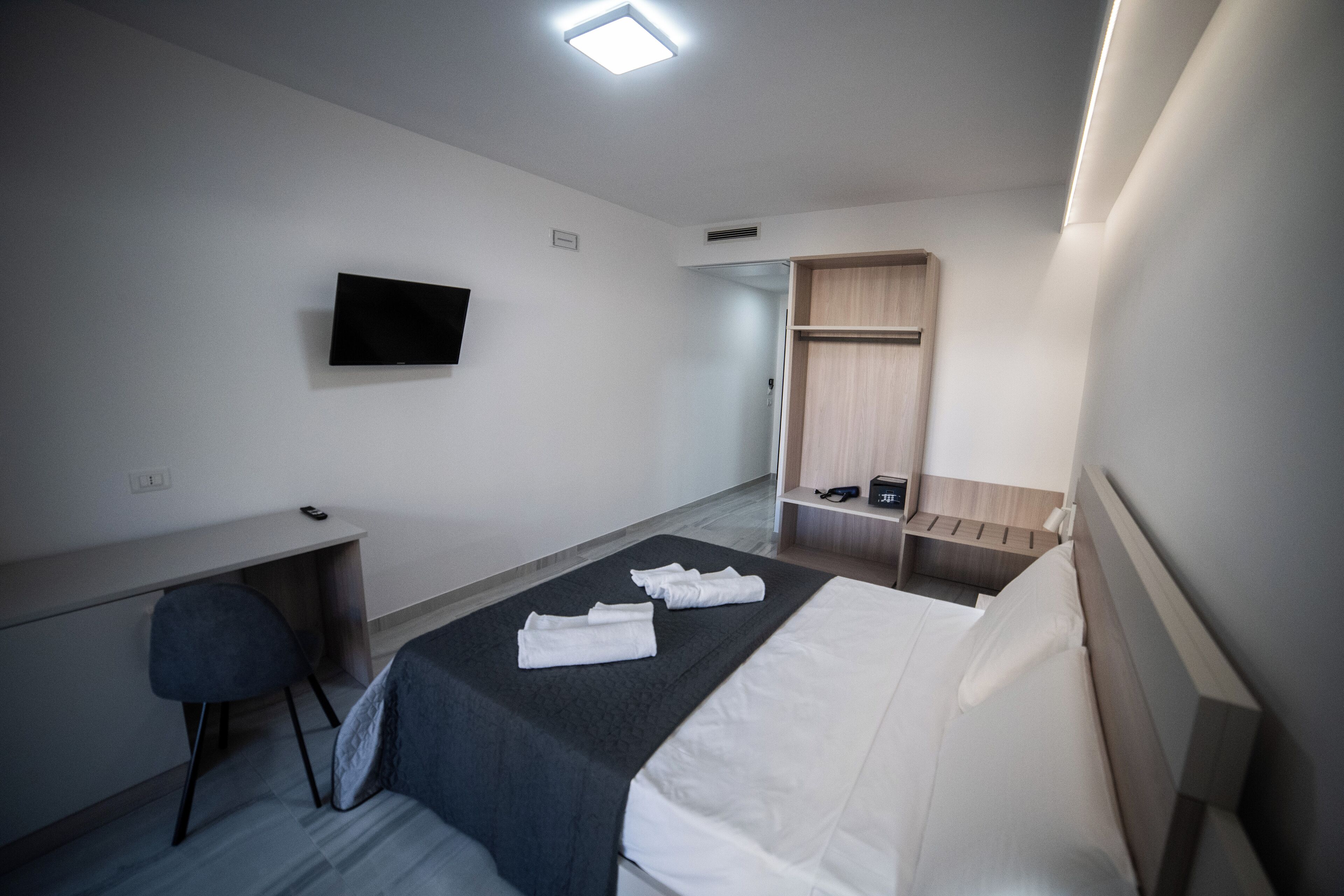 Een hotelkamer met een bed, bureau, stoel, televisie en een kledingkast.