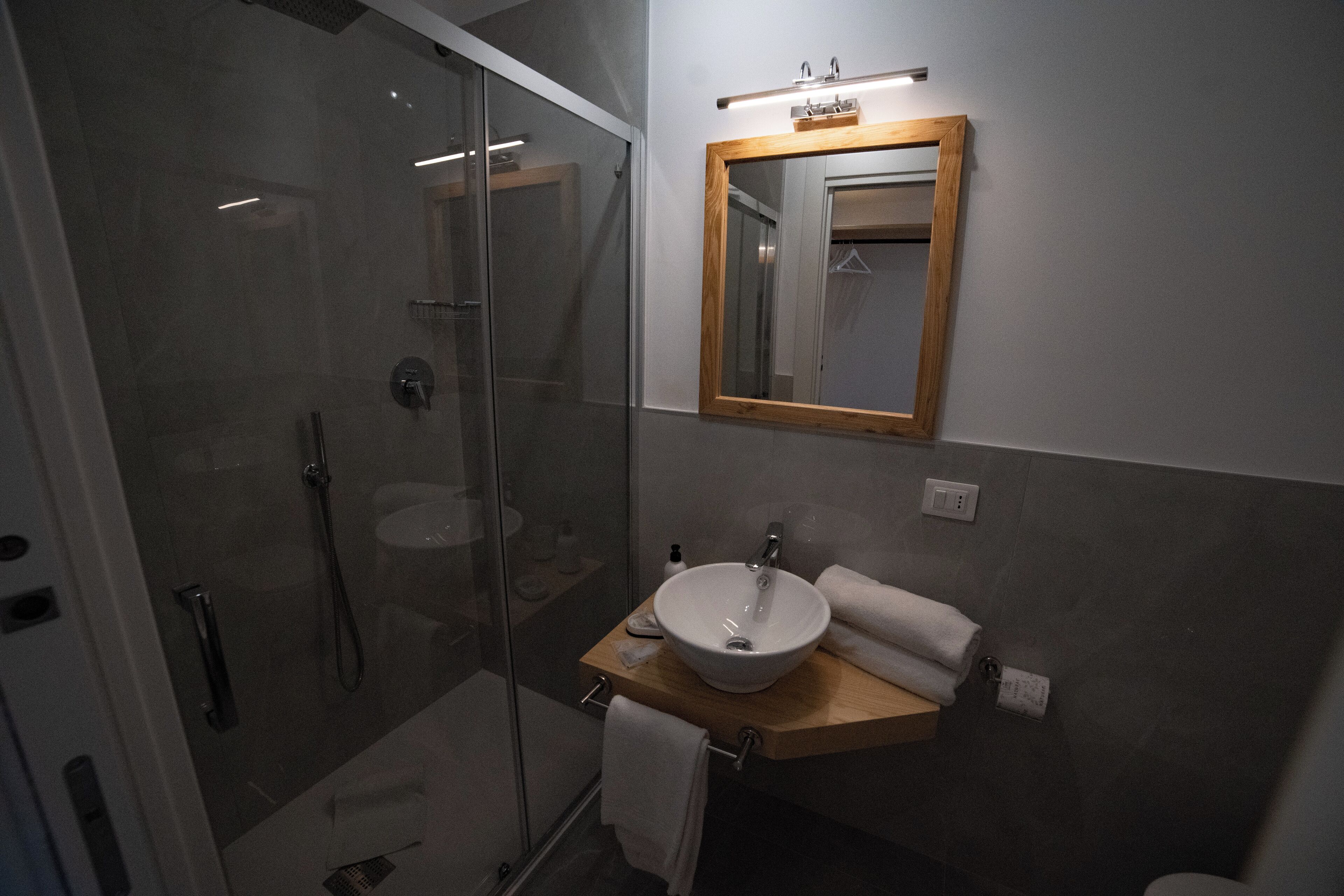 Un bagno moderno con doccia vetrata, un mobile bagno in legno con lavandino bianco e uno specchio sopra il lavandino.