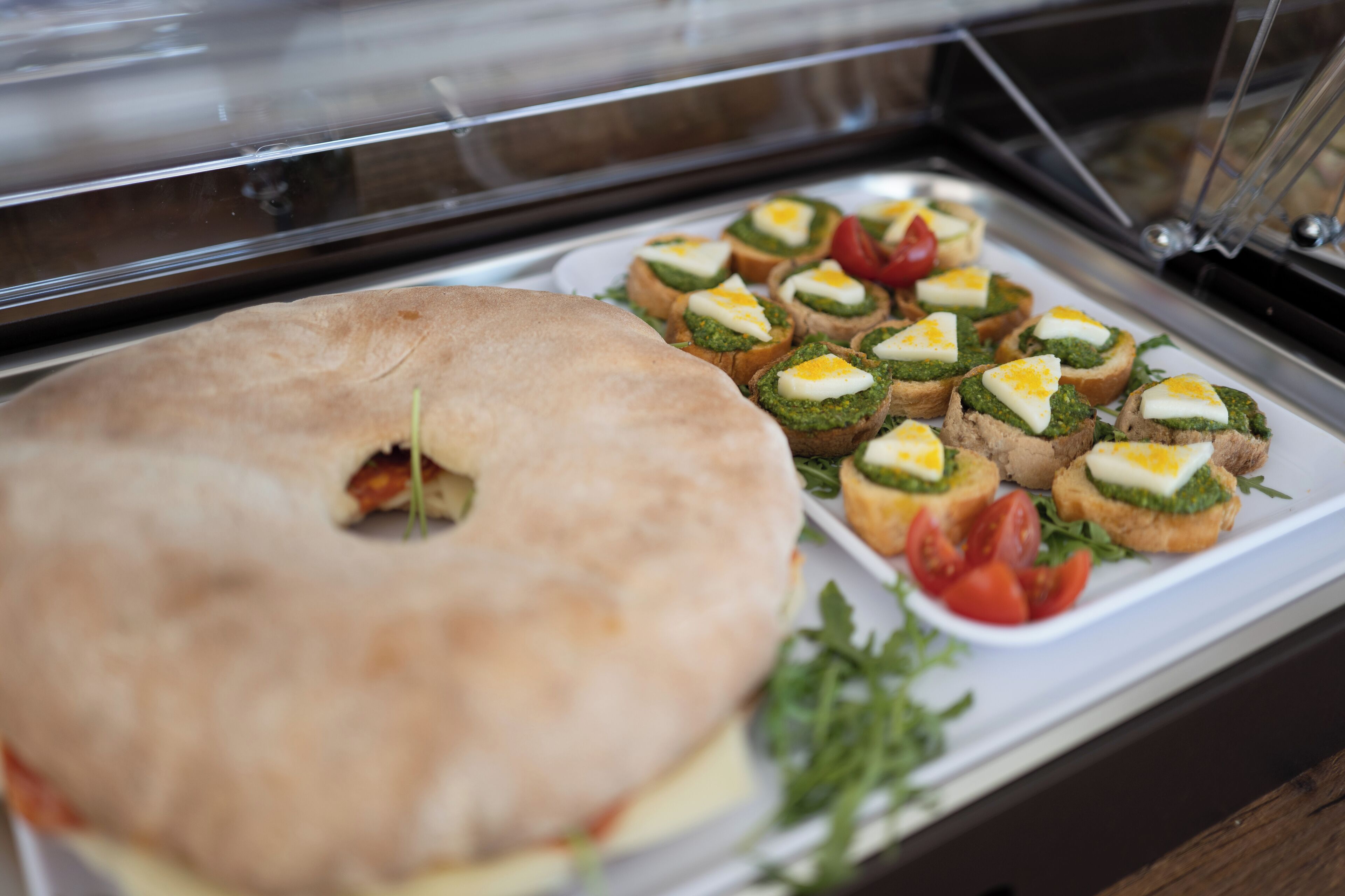 Un buffet con una varietà di cibi, tra cui un bagel grande, panini con uova e un piccolo piatto di pomodori a fette.