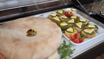 Un buffet con una varietà di cibi, tra cui un bagel grande, panini con uova e un piccolo piatto di pomodori a fette.