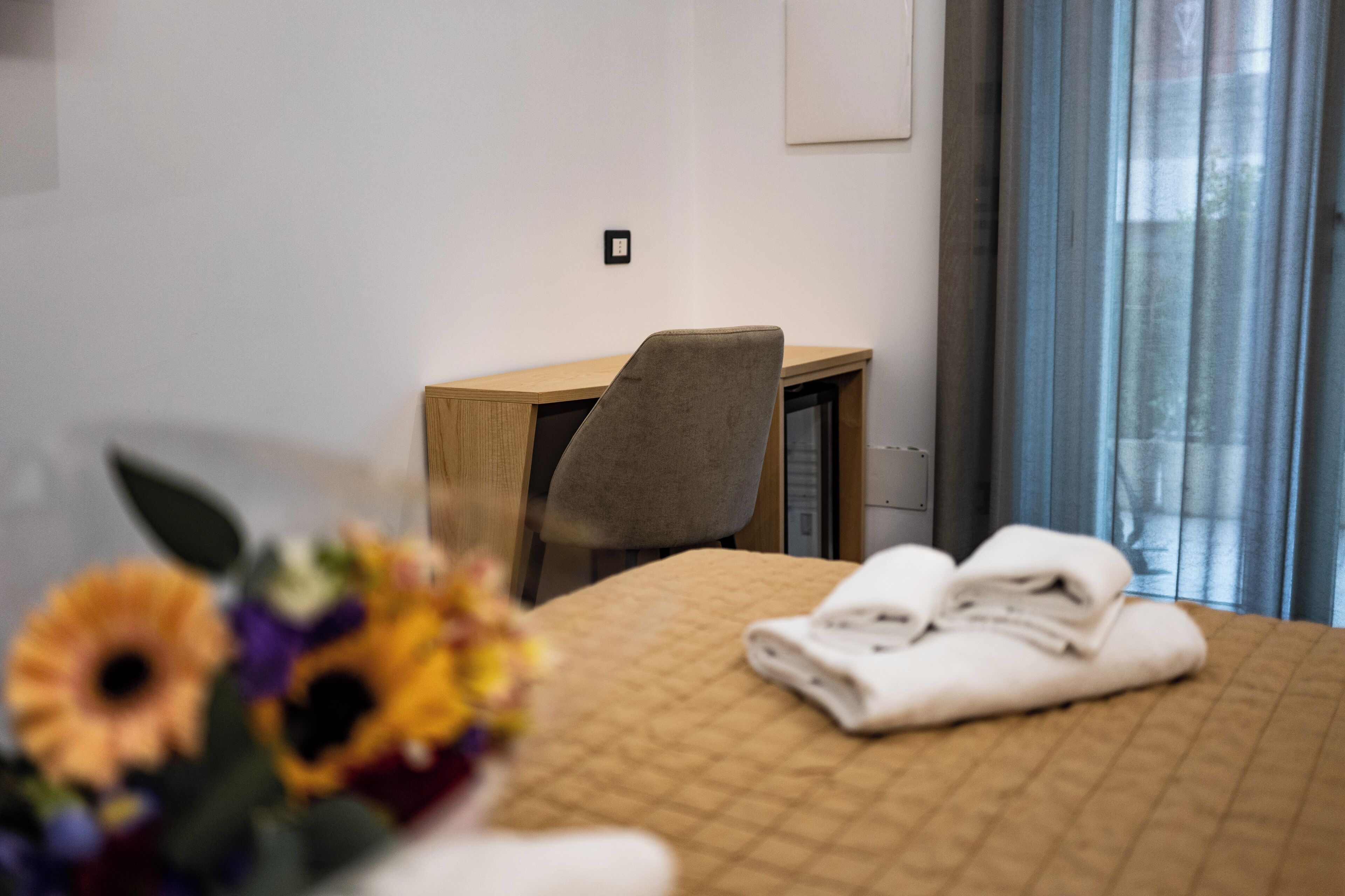 A hotel room with a bed, a desk, a chair, and a window with curtains.