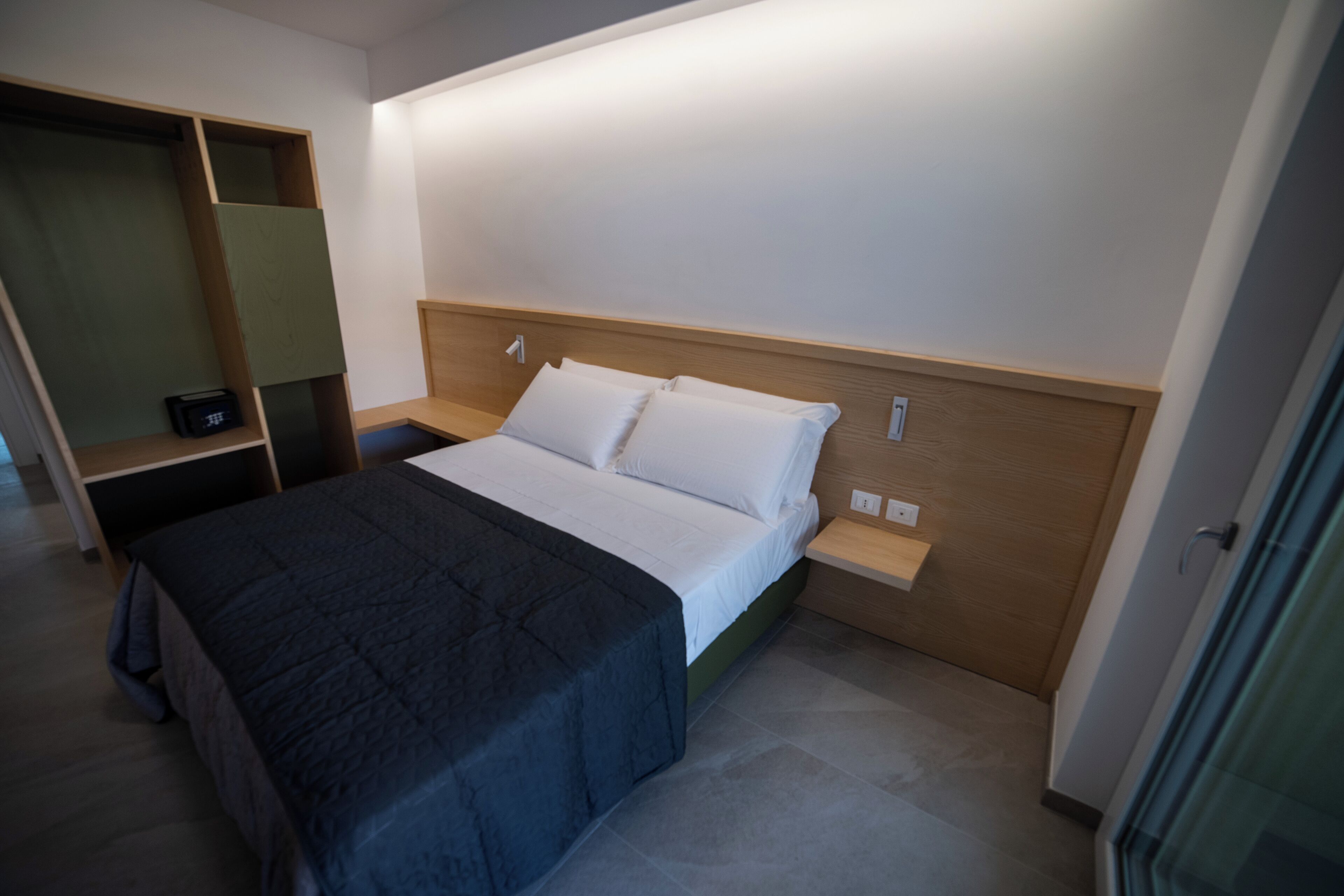 Une chambre d’hôtel moderne avec un lit bien fait, une tête de lit en bois et une étagère intégrée.