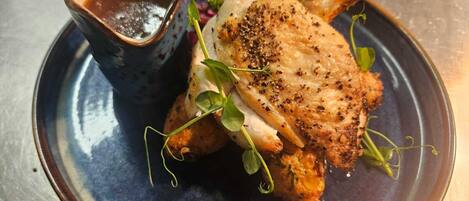 A plate with a roasted chicken and a small bowl of sauce.