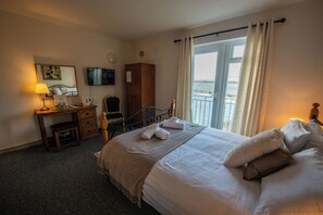 A hotel room with a bed, a desk, a chair, a TV, and a view of the sea. - Greenfield Lodge Hotel Bar & Bistro (Headford)
