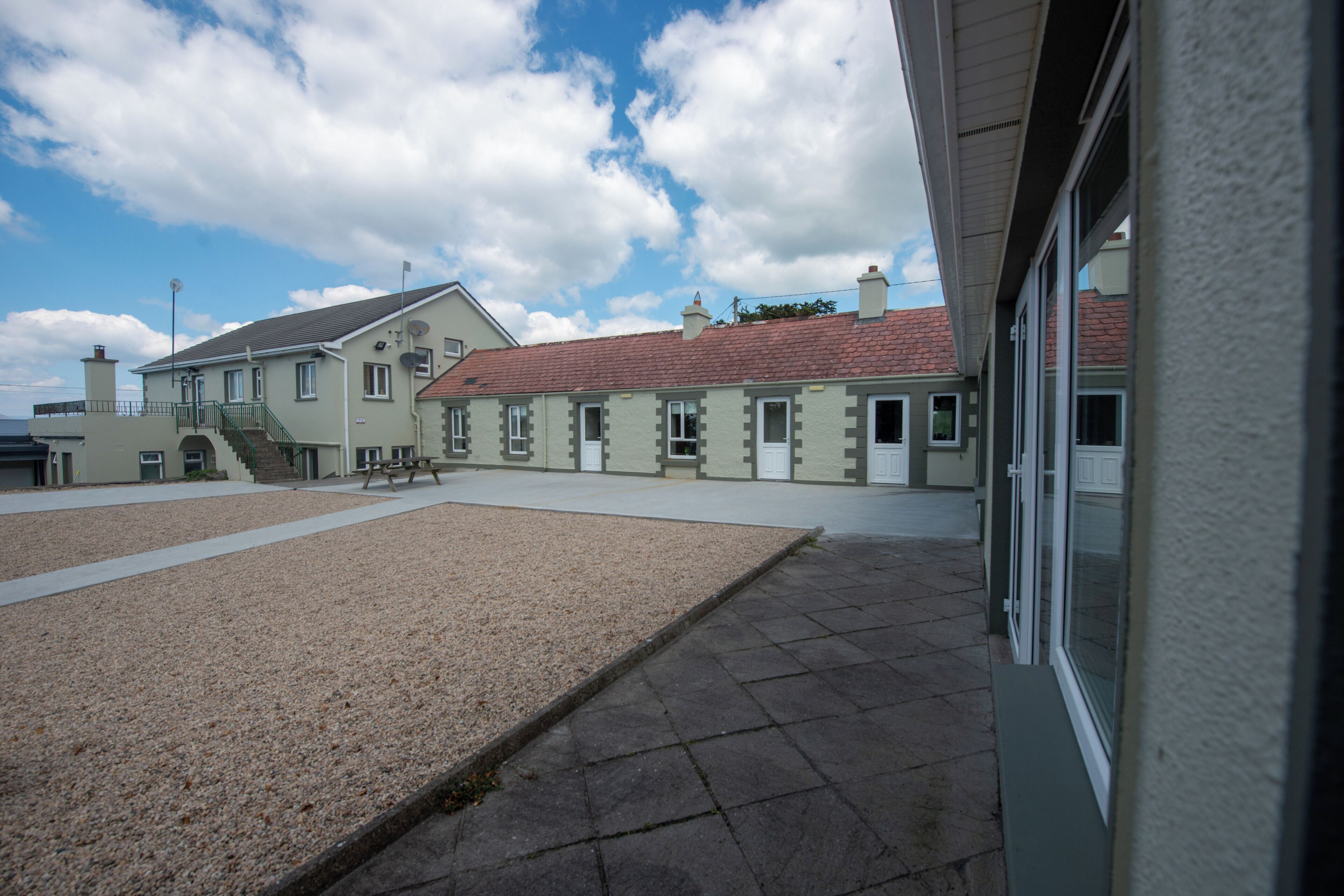 A building with a gravel courtyard, a staircase leading to a second floor, and a red-tiled roof.