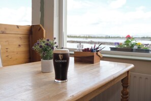 A wooden table with a glass of Guinness beer, a potted plant, and a view of a body of water through a window. - Greenfield Lodge Hotel Bar & Bistro (Headford)