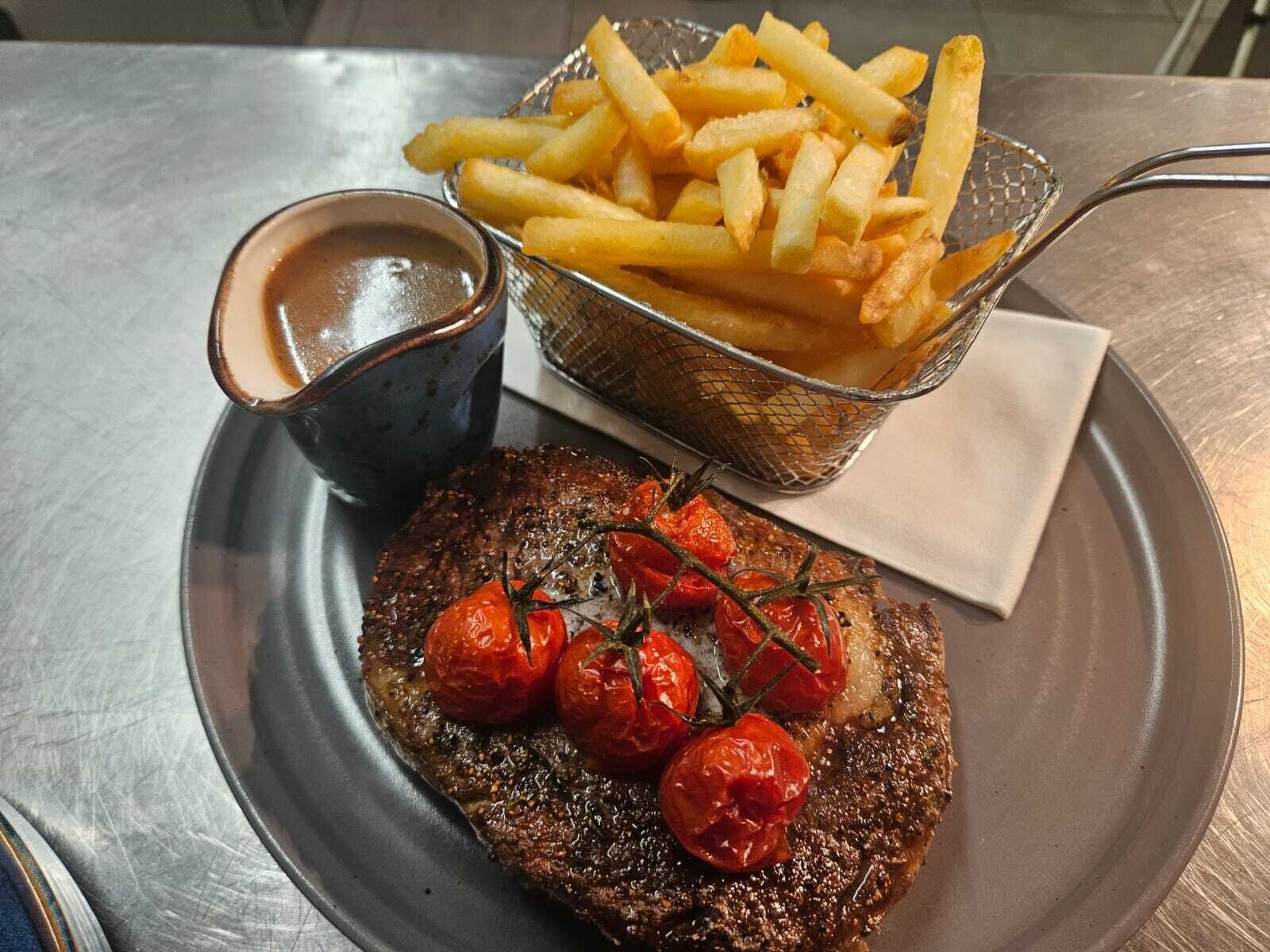Une assiette avec un steak garni de tomates cerises et accompagnée de frites.