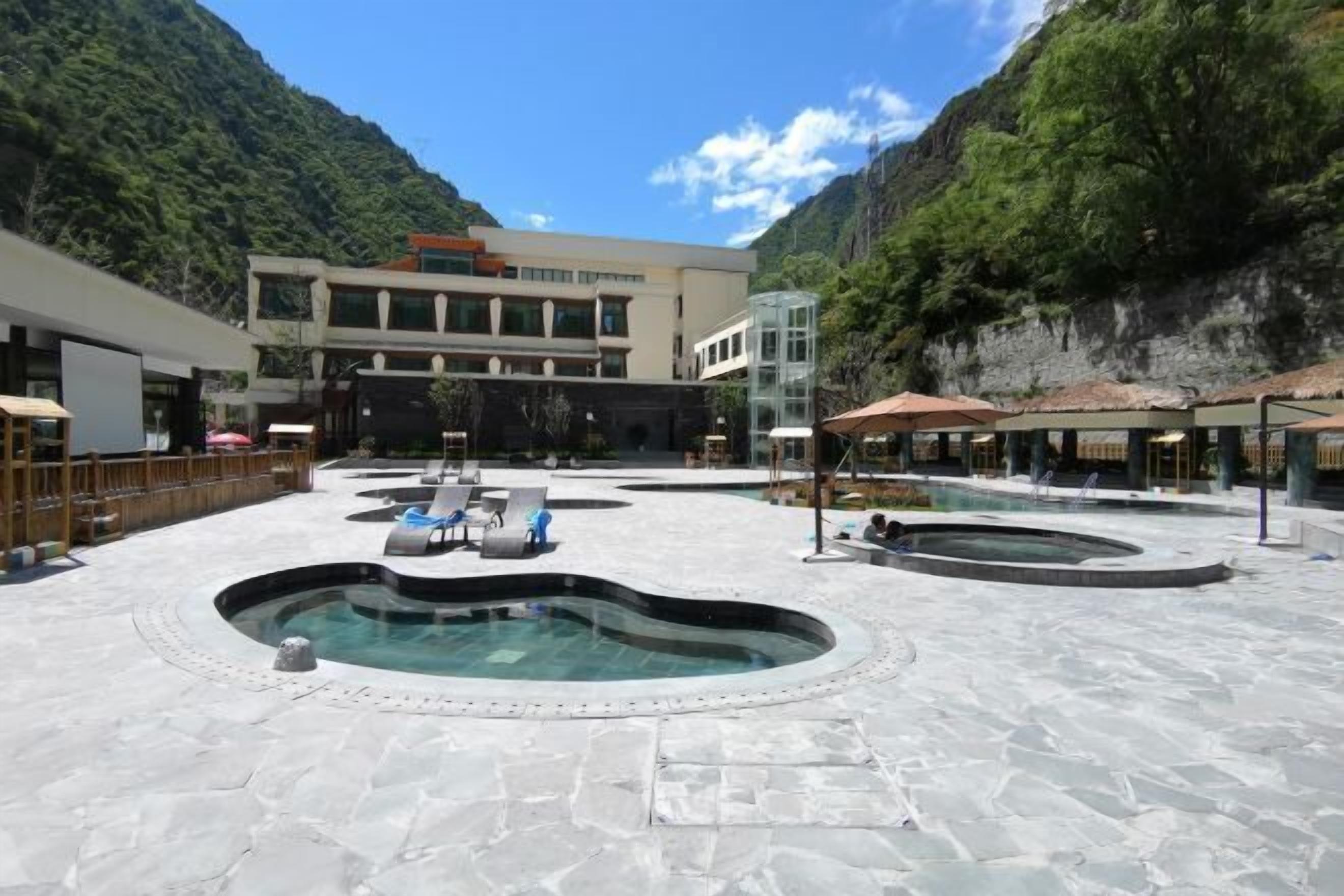 A pool area with multiple hot tubs and lounge chairs, surrounded by a building with a modern design and a mountainous backdrop.