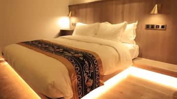 A neatly made bed with a patterned blanket and pillows, wooden headboard, bedside lamps, and a control panel on the wall.