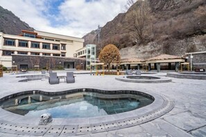 A pool area with a hot tub, lounge chairs, and a building with a modern design. - Gu Er Gou Hot Spring Resort (Li County)