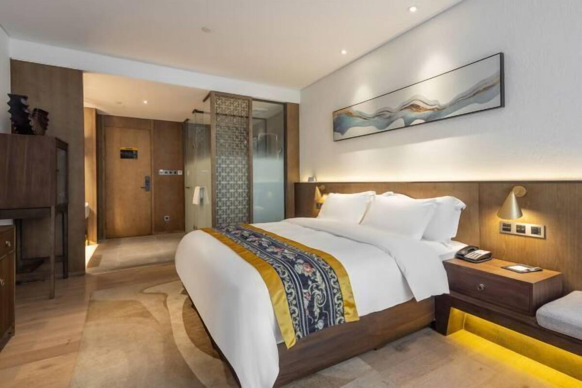 A modern hotel room with a large bed, bedside table, and a wall-mounted artwork.