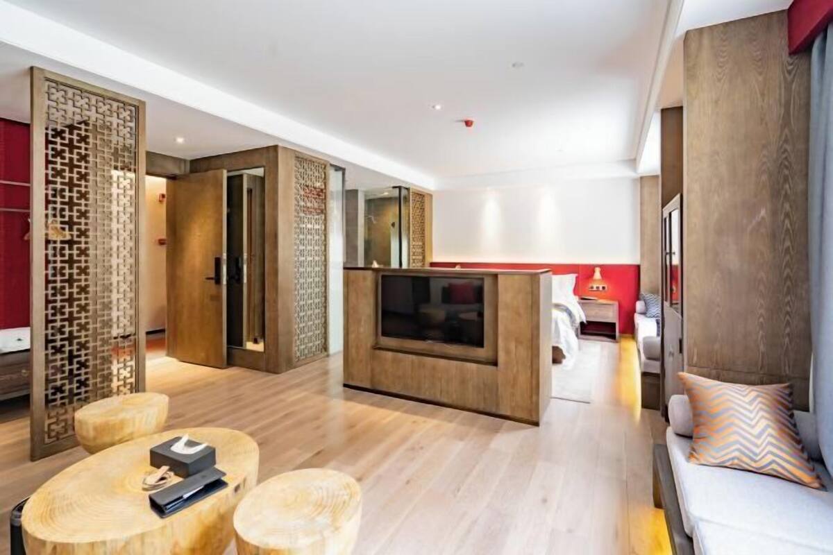 A modern hotel room with a wooden floor, a sofa, a TV, and a decorative screen.