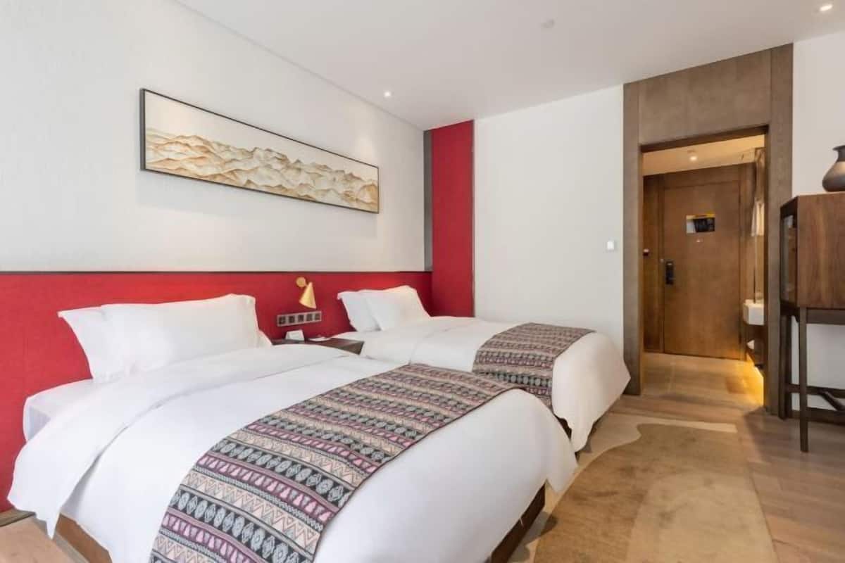 A hotel room with two beds, a red accent wall, a framed artwork, and a wooden door.