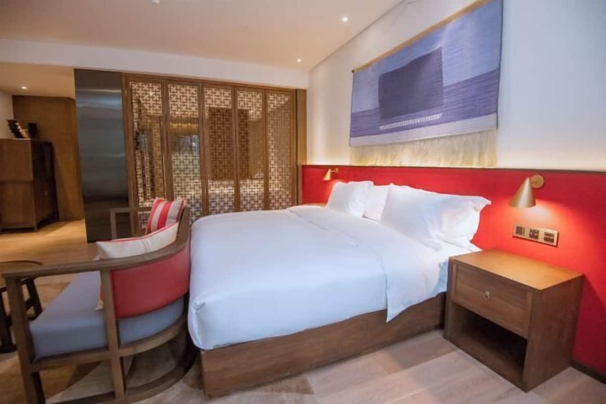 A hotel room with a bed, bedside table, nightstand, and a desk with a chair.